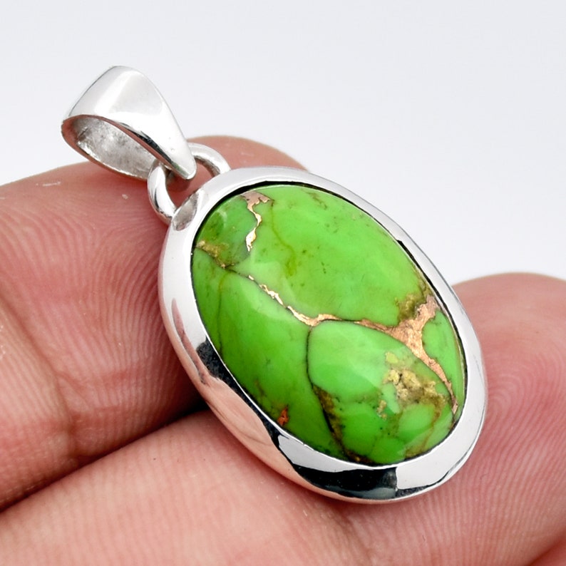 May include: A silver pendant with a green oval turquoise stone with copper veins. The stone is set in a silver bezel.