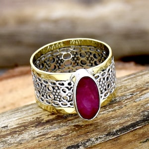 May include: A silver ring with a gold band and a large oval ruby gemstone. The ring features a delicate filigree design.