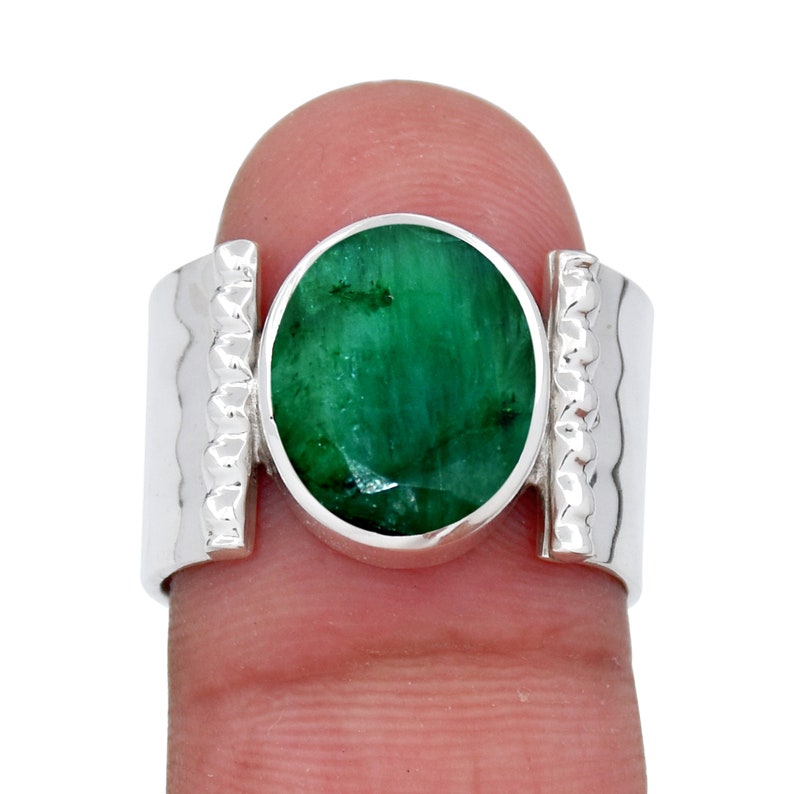 Puede incluir: Un anillo de plata con una gran esmeralda de forma ovalada. El anillo tiene una banda texturizada con una secci&oacute;n rectangular elevada a cada lado de la piedra.