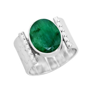 Puede incluir: Un anillo de plata con una gran esmeralda de forma ovalada engastada en el centro. La banda del anillo es texturizada y tiene un acabado martillado.
