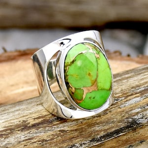 May include: A silver ring with a green and gold oval turquoise stone set in a modern design.