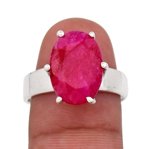 Peut inclure: Une bague en argent ornée d'une grosse pierre précieuse rubis de forme ovale. Le rubis est d'une couleur rouge vif. Le corps de la bague est en argent poli. La pierre est maintenue par quatre griffes.