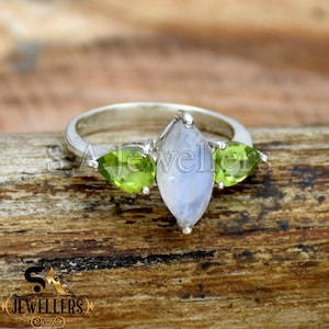 Puede incluir: Un anillo de plata con una gran piedra de luna en forma de pera y dos piedras de peridoto verdes más pequeñas en forma de pera.