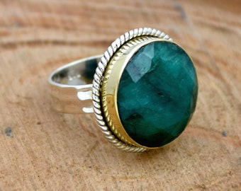 May include: A silver ring with a gold band and a large, faceted emerald green gemstone.