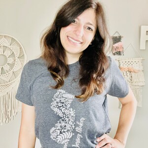 May include: A gray t-shirt with a white floral design of the state of New Jersey and the text "Jersey Maker".