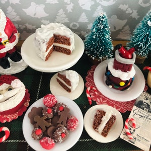 Pode incluir: Uma cena de Natal em miniatura com um bolo branco coberto de glacê, uma casa de gengibre e figuras do Papai Noel. Há também bengalas de doces, um jornal com a manchete "Gingerbread" e um prato de homens de gengibre de chocolate.