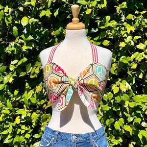 May include: A halter top with a peace sign pattern in shades of green, yellow, pink, and blue. The top is tied in a bow at the front.