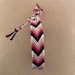 May include: A pink, white, and black friendship bracelet with a chevron pattern.