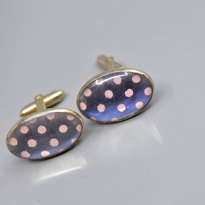 May include: A pair of oval-shaped cufflinks with a gold metal frame and a blue background with pink polka dots.