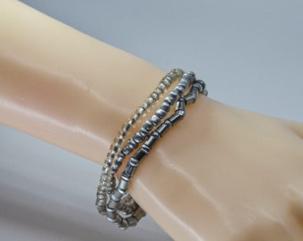 May include: Three beaded bracelets stacked on a wrist. The top bracelet is made of clear beads, the middle bracelet is made of silver beads, and the bottom bracelet is made of black beads.