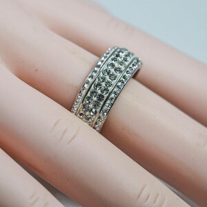 May include: A silver ring with three rows of clear cubic zirconia stones.