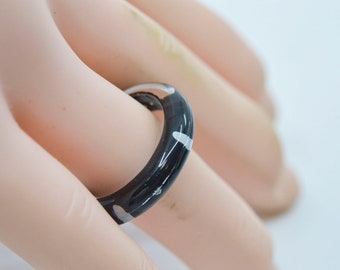 May include: A black ring with white accents. The ring is made of a smooth, shiny material.