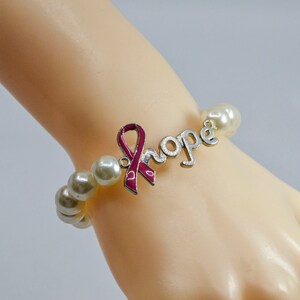 May include: A pearl bracelet with a silver charm that says "hope" and features a pink ribbon.