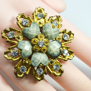 May include: A gold-tone flower brooch with five white and grey heart-shaped stones surrounded by clear rhinestones.