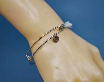 May include: A silver bangle bracelet with a white tassel charm and a small silver disc charm.