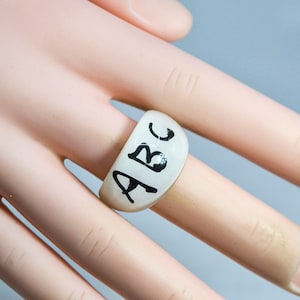 May include: White ring with the letters "ABC" written in black ink.