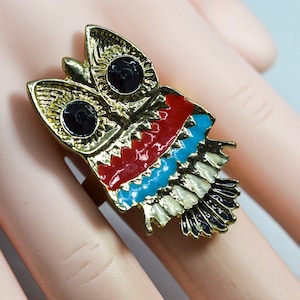 May include: A gold owl ring with red, blue and white enamel accents. The owl's eyes are black.