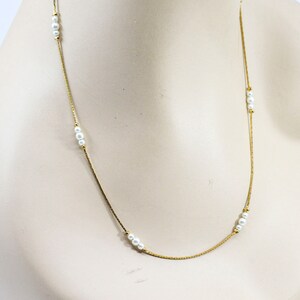 May include: A gold chain necklace with white pearl accents. The necklace is on a white mannequin.