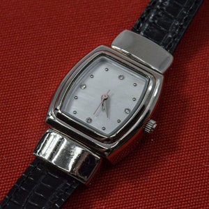 May include: A silver watch with a white face and black leather band. The watch has a rectangular face with a silver bezel and a black leather band.