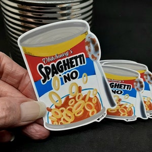 May include: Two red, white, and blue stickers with the text "Obitchuary's Spaghetti-O's No" and "Obitchuary's Ghetti-O's No" and a cartoon image of a can of spaghetti-o's with a spoon.