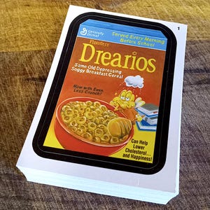May include: A stack of trading cards featuring a parody cereal box design. The card reads "Drearios" with the tagline "Same Old Depressing Soggy Breakfast Cereal." The card also states "Now with Even Less Crunch!" and "Can Help Lower Cholesterol... and Happiness!"