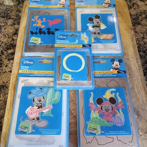May include: Several Disney-themed die-cut and embossing sets featuring Mickey Mouse and related characters. Each set includes a cutting folder and embossing folder. The sets have blue and silver packaging.
