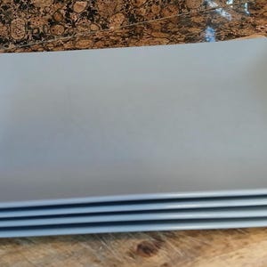May include: A stack of four rectangular plates in a solid light blue color. Each plate features rounded corners and a smooth, matte finish. The plates are uniform in size and shape, stacked neatly on top of one another to create a single vertical unit.