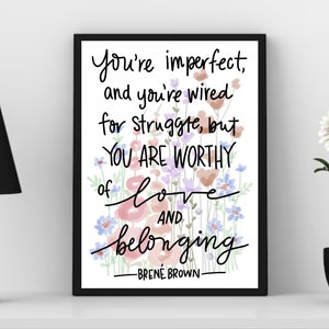 May include: A black framed print with a white background and a quote by Brené Brown that reads "You're imperfect, and you're wired for struggle, but YOU ARE WORTHY of love AND belonging -BRENÉ BROWN-". The quote is surrounded by watercolor flowers in shades of pink, blue, and green.