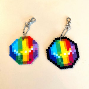 Peut inclure: Deux porte-clés pixelisés aux couleurs de l'arc-en-ciel. Chaque porte-clés est doté d'un fermoir et d'une chaîne de couleur argentée. L'un des porte-clés a une bordure noire, l'autre une bordure aux couleurs de l'arc-en-ciel.
