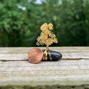 May include: A miniature wire tree sculpture with a gold finish, standing on a black stone base. A penny is placed in front of the sculpture for scale.