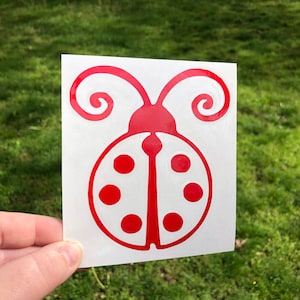 May include: Red ladybug sticker with white spots and curled antennae. The sticker is on a white background.