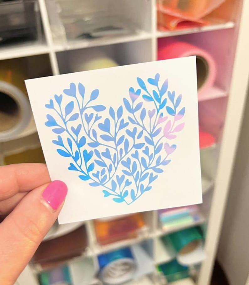 May include: A square white sticker featuring a heart-shaped design composed of blue and light purple botanical branches with small leaves. The sticker displays a gradient color effect transitioning from deep blue to soft purple across the foliage.