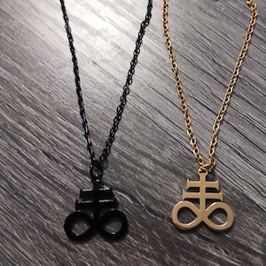 May include: Two necklaces with pendant charms. One necklace is black, the other is gold. Each necklace has a chain and a pendant with a symbol. The pendants are the same shape, a cross above an infinity symbol.