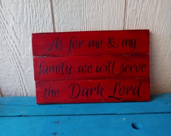 May include: Red wooden sign with the text "As for me & my family, we will serve the Dark Lord" in black cursive lettering.