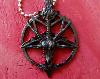 Könnte beinhalten: Schwarze Metallkette mit einem Anhänger, der einen Ziegenkopf mit Hörnern in einem Pentagramm zeigt. Der Anhänger ist an einer silbernen Kette befestigt.