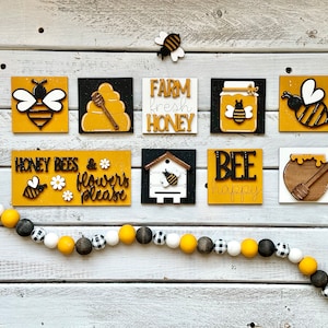 May include: A set of nine wooden signs with bee and honey themed designs. The signs are painted in yellow, black, and white with phrases like "Honey Bees & Flowers Please", "Farm Fresh Honey", and "Bee Happy".