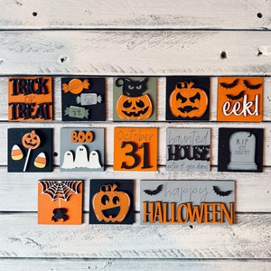May include: A collection of Halloween-themed wooden blocks. Each block features a different design, including pumpkins, bats, candy, ghosts, and the phrases "Trick or Treat," "Boo," "October 31," "Haunted House," "Eek!," and "Happy Halloween."