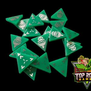 May include: A set of 13 green triangular dice with silver skull and arrow designs. The dice are scattered on a black background. The dice are for a game called "Top Rope Games".