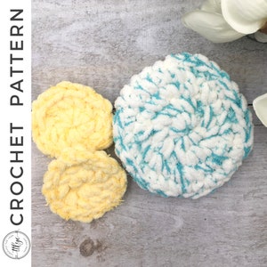 May include: Three crocheted flower shapes, one is yellow, one is white with blue accents, and one is a lighter yellow. The flowers are on a light wood background.