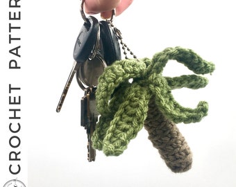 May include: A crocheted palm tree keychain in green and brown. The keychain is attached to a set of keys.