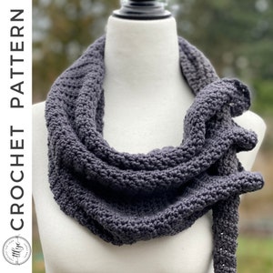 May include: A dark gray crocheted infinity scarf, displayed on a white mannequin. The scarf is made with a simple stitch pattern and has a long, flowing shape.