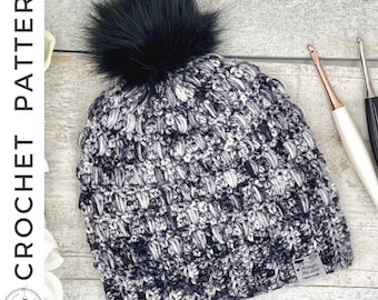 May include: A black and white crochet beanie with a black faux fur pom pom. The beanie has a tag that says "Through The Loop - Yarn Crafts".