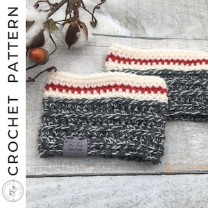 May include: Two gray and white crocheted cup cozies with a red and white stripe detail. The cozies are on a white wooden surface. The label on one of the cozies reads "Through The Loop - Yarn Craft".