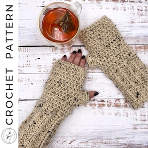 May include: A pair of beige crochet fingerless gloves with black flecks. The gloves are on a white wooden surface.