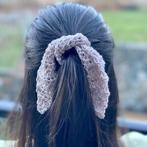 May include: A light purple crocheted hair scrunchie tied in a bow around a ponytail.