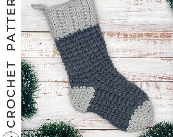 May include: A handmade crochet Christmas stocking in shades of gray. The top and toe are light gray, while the body is a darker gray. The words "CROCHET PATTERN" are printed vertically on the left side of the image.