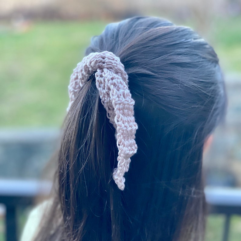 May include: A light pink crocheted hair scrunchie tied around a ponytail.