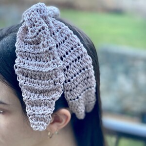 May include: A light pink crocheted headband with a bow design. The headband is made with a delicate, open stitch pattern.