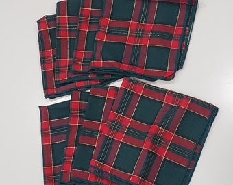 May include: A set of eight folded square cloth napkins. The napkins feature a classic plaid pattern in red, green, and gold. The napkins are arranged in two stacks, with four napkins in each stack.