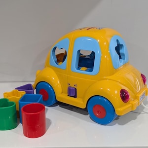May include: A yellow toy car with blue window frames and red and blue wheels. The car has shape sorter cutouts and comes with various coloured shape blocks. A fun educational toy for toddlers.